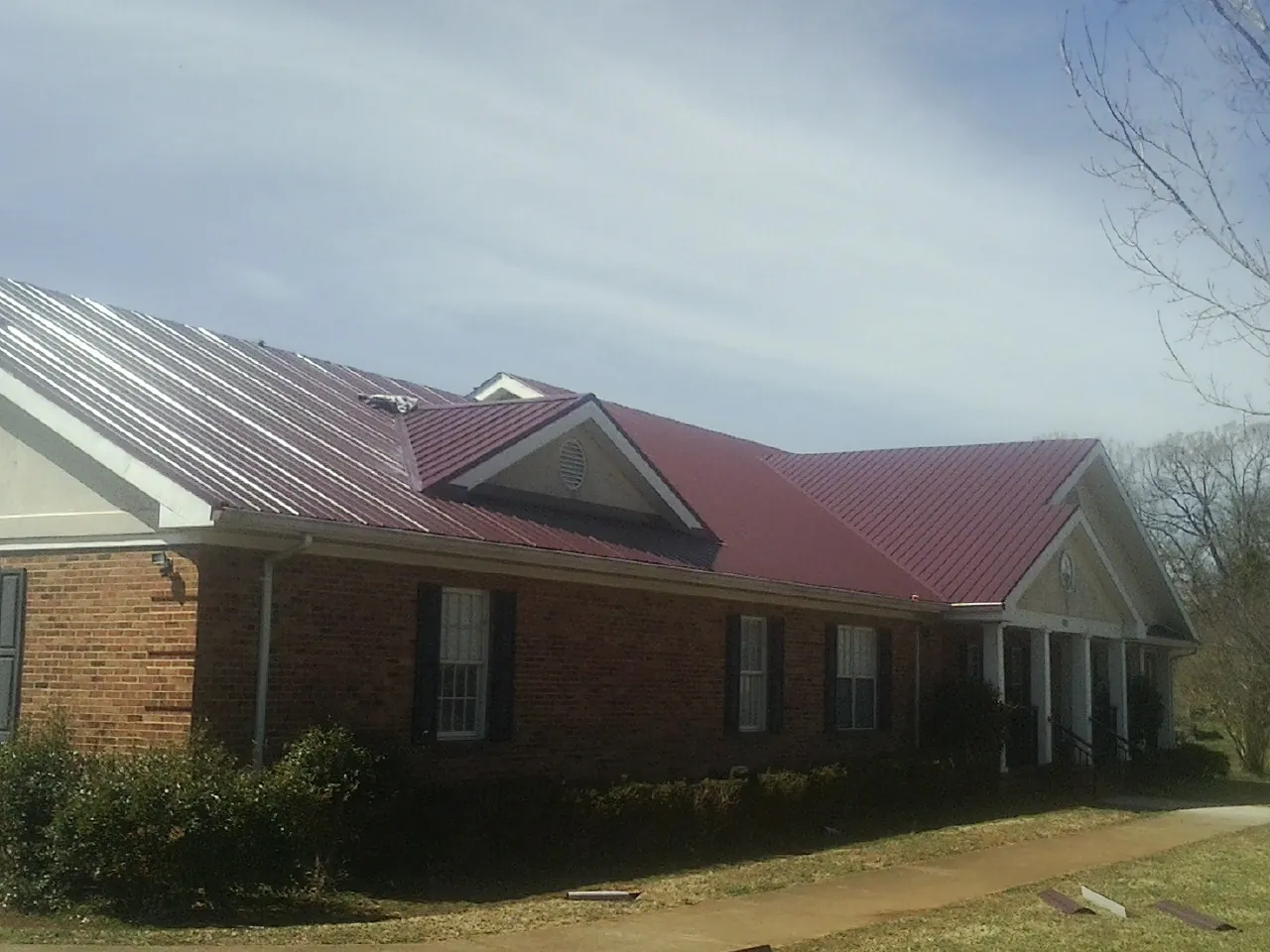 Red metal roof with gabled entries on a long brick building, from a Hail Damage Roof Repair job in Tillamook