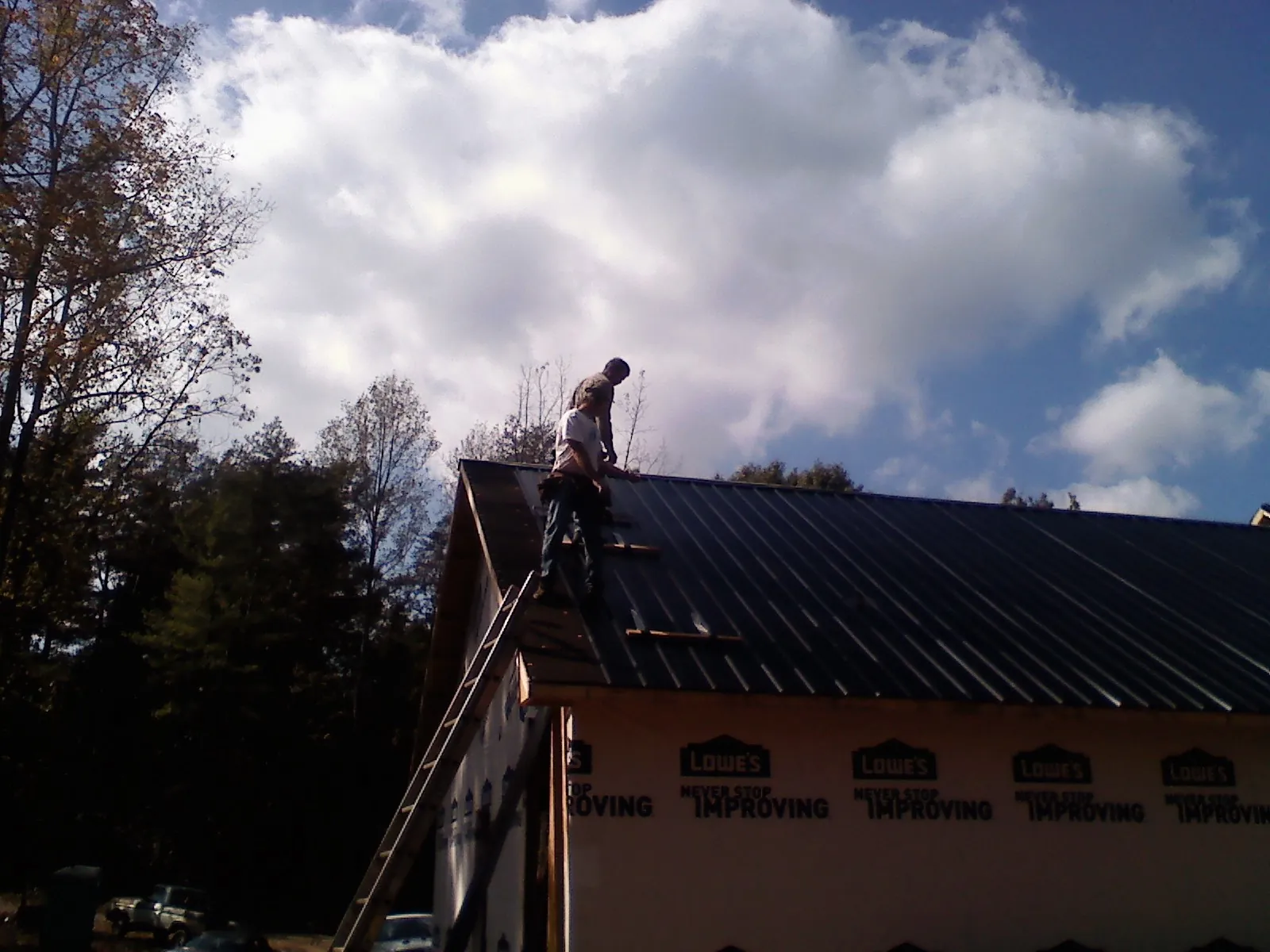 Roofer fastening dark metal panels high against a cloudy sky, from a Roof Inspection job in Tillamook
