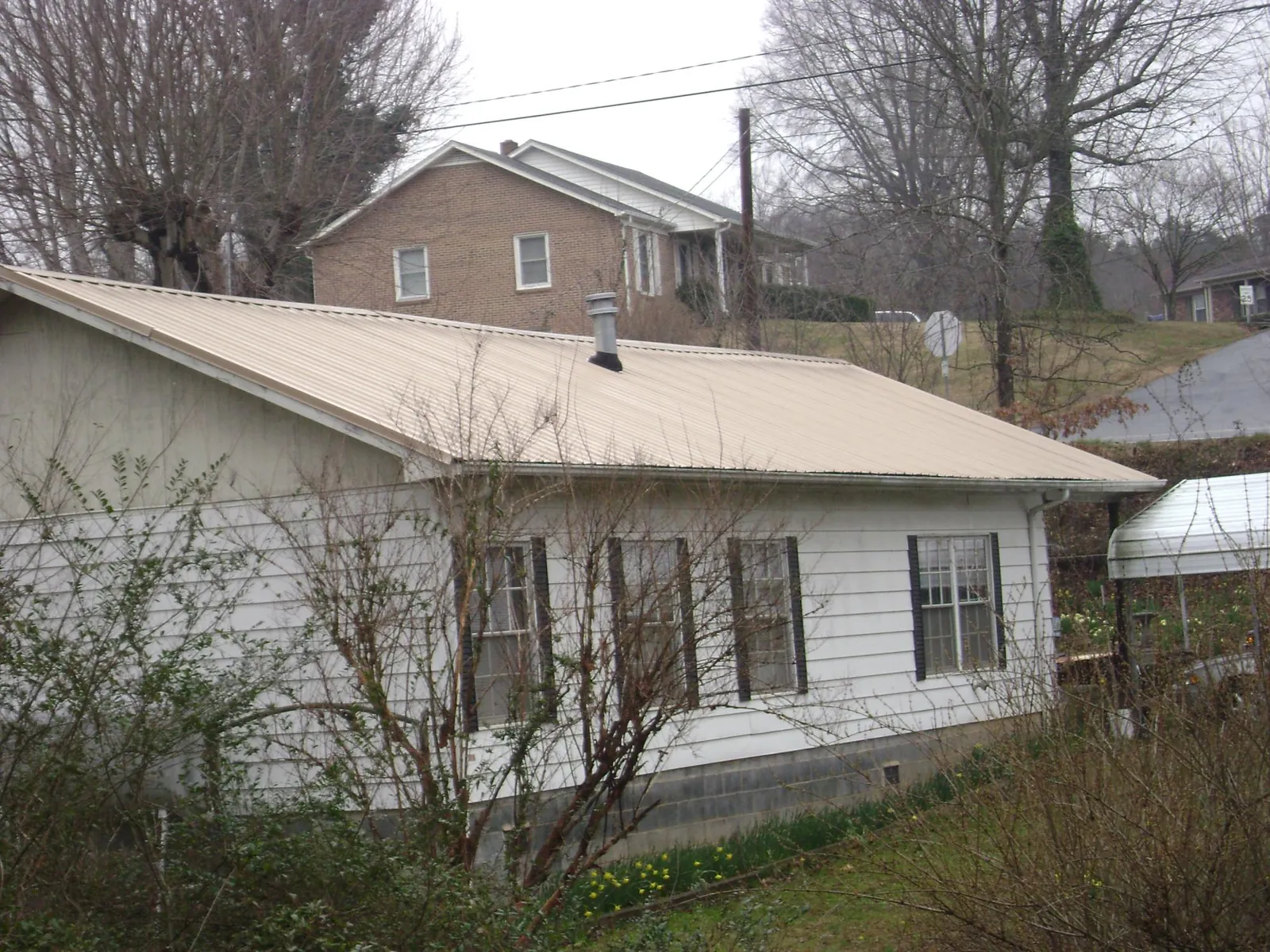 Tan metal roof on a white sided house set into a hillside — Commercial Roofing by Roofing Brothers in Tillamook
