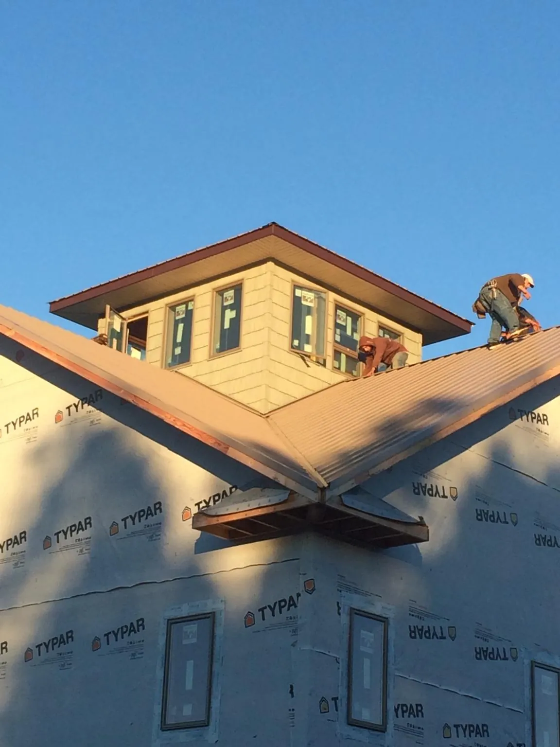 Roofers working around a rooftop cupola on a new metal roof at sunset — Roof Waterproofing in Tillamook by Roofing Brothers
